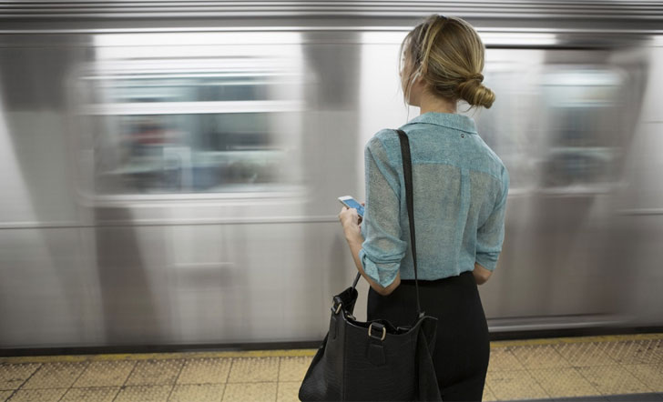 Una mujer espera la llegada del metro con su móvil en la mano