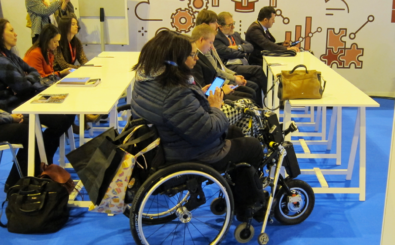 Una mujer en silla de ruedas mira su móvil durante un taller sobre accesibilidad de las personas con movilidad reducida, es uno de los talleres de Fitur sobre accesibilidad en los destinos turísticos inteligentes.