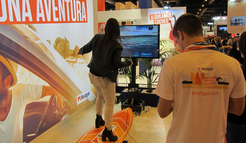 Una joven prueba un simulador de surf subida a una tabla y mirando una pantalla como atracción de Fitur para los destinos turísticos inteligentes.