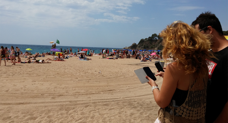 El acceso a Internet a través de wifi en la playa de Lloret (Gerona) es público y gratuito desde hace unos días. Dos personas utilizan sus teléfonos inteligentes en la playa de Lloret.