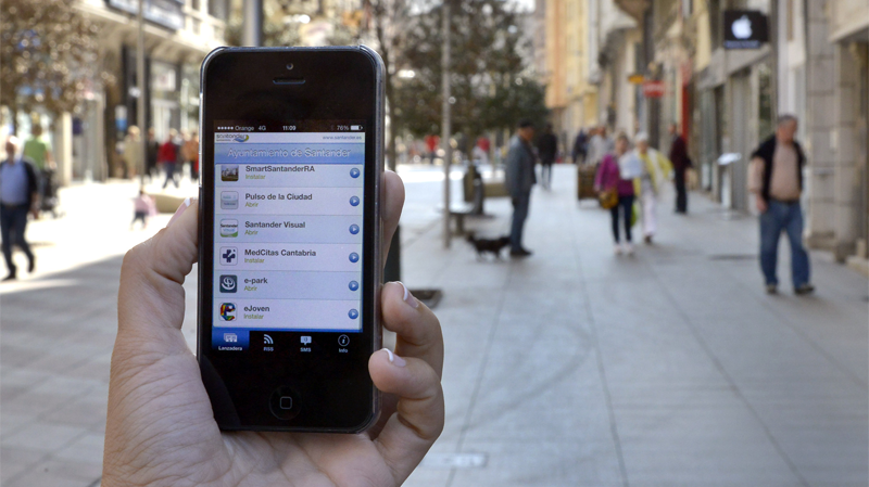 Una mano sostiene un teléfono móvil inteligente con aplicaciones sobre un fondo de una calle llena de gente