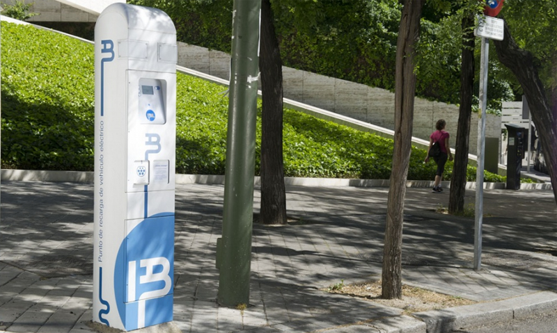 Punto de recarga para vehículo eléctrico situado en la acera de una calle.