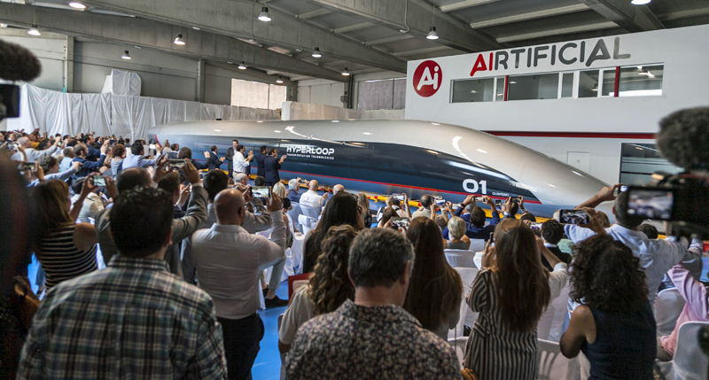 muchas personas asisten a la presentación de la cápsula de pasajeros de Hyperloop, que se encuentra en segundo plano.