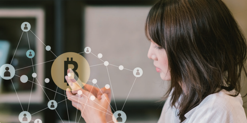 Mujer maneja un smartphone en el que se supone, por el símbolo de bitcoin sobreimpreso en la imagen y la red de contactos que aparece, que está haciendo una transacción bancaria.
