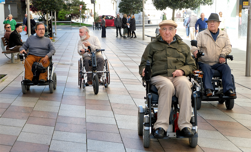 Un grupo de cuatro personas en sillas de rueda eléctricas circulan por una calle de Santander.