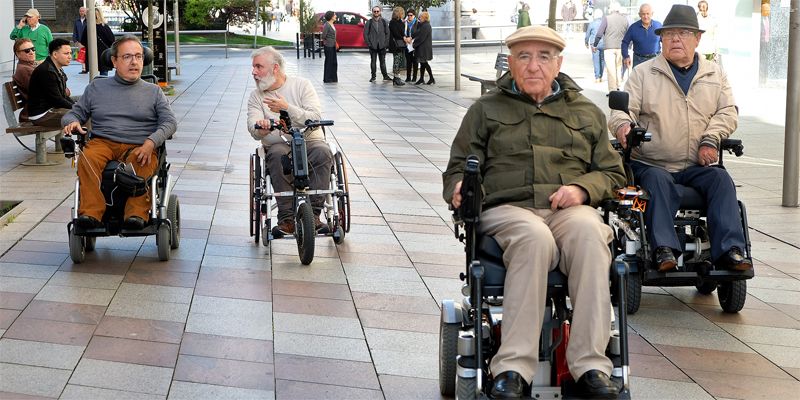 Un grupo de cuatro personas en sillas de rueda eléctricas circulan por una calle de Santander.
