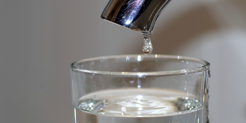 Grifo cerrado del que sale una gota de agua que va a caer en un vaso con agua