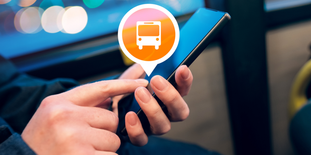 Unas manos manejan un teléfono móvil inteligente en un autobús y aparece el símbolo de un vehículo de transporte público.